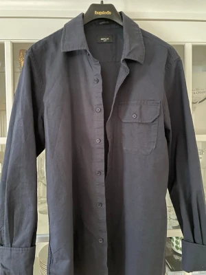 Mörkblå skjorta från Replay - Stilren mörkblå skjorta från Replay med klassisk krage och bröstficka med knapp. Skjortan har långa ärmar och knäppning framtill. Perfekt för dig som gillar en enkel och tidlös look.