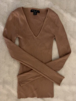 Beige ribbstickad tröja AMISU - Säljer en beige ribbstickad tröja från AMISU med djup V-ringning och långa ärmar. Tröjan är figurnära och har en mjuk, stretchig känsla som passar perfekt till jeans eller kjol. Materialet är en blandning av viskos och polyamid.