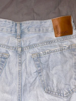 Ljusblå straight jeans från Bikbok - Säljer ett par ljusblå straight fit jeans från BikBok med mid midja. Jeansen har bälteshällor, knappgylf och en snygg läderpatch bak i midjan. Perfekta för en avslappnad och trendig look. Lite skrynkliga då dom knappt använts. Fler bilder kan skickas.