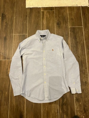 Ralph Lauren Skjorta - Säljer denna stilrena skjortan från Ralph Lauren med färgen ljusblå! Gjort av 100% bomull och har storleken S! Sitter riktigt snyggt och bekvämt vilket gör att den passar riktigt bra till många outfits! Vid funderingar och frågor är det bara att höra av sig! Pris kan såklart diskuteras vid snabb affär! 