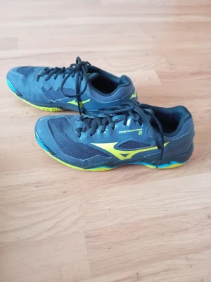 Mizuno Wave Phantom 2 inomhusskor - Säljer ett par Mizuno Wave Phantom 2 inomhusskor i mörkblått med neongula och blå detaljer. Skorna har snörning, ventilerande meshpaneler och slitstark sula som passar perfekt för sporter inomhus. Snygg design med Mizuno-logga på sidan. Inköpt: 1500kr
