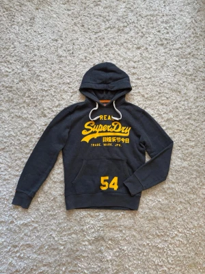 Blå hoodie från superdry - Snygg mörkblå hoodie från superdry. Den är använd men i toppskick utan defekter. Storlek S!