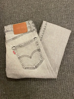 Grå slim Levi's jeans av model 502 med tapered ben - Snygga grå slim Levi's jeans av model 502 i storlek 28/32 med klassisk femficksdesign och tapered ben. Lite små i storleken. Jeansen har små slitningar på vissa ställen, bl.a. grenen och fickorna (se exempel på bild 4 och 5)
