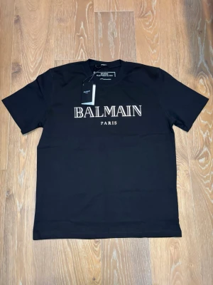  Balmain t-shirt - Snygg svart t-shirt från Balmain med klassisk vit logga på bröstet. T-shirten har rund halsringning och korta ärmar. Tillverkad i mjuk bomull för en skön känsla och stilren look.     Den är helt ny aldrig använd  unik 