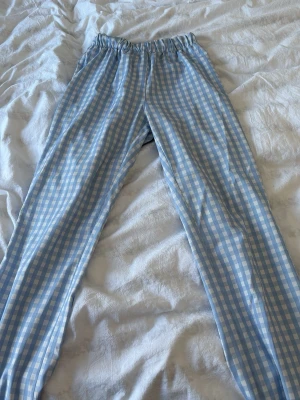 Blårutiga pyjamasbyxor med resårmidja - Säljer ett par pyjamasbyxor från design by si i ljusblått och vitt rutmönster. Byxorna har resår i midjan och raka ben, samt två bakfickor.  Materialet är mjukt och luftigt. Storlek S. Använd fåtal gånger. 