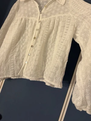 Vit broderad blus med knappar - Söt vit blus med broderade blommor och genombrutet tyg. Blusen har krage, knäppning framtill och långa puffiga ärmar. Perfekt för alla tillfällen. Pris kan diskuteras. Använd kanske en eller två gånger.