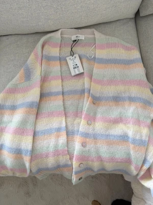 Pastellrandig kofta från Gina Tricot - Kofta från Gina Tricot i ullblandning. Koftan har breda pastellfärgade ränder i rosa, blått, gult, grönt och orange. V-ringad med knappar. Helt ny prislapp kvar. Inköptes i somras.