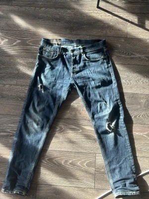  Dondup jeans - Säljer ett par blå jeans från Dondup med snygga slitningar och hål på benen. Jeansen har klassisk femficksmodell och är tillverkade i denim. Perfekta för dig som gillar en avslappnad och trendig stil.
