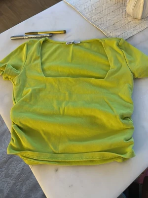 Limegrön topp med fyrkantig ringning - Trendig limegrön topp från ZARA med fyrkantig ringning och korta ärmar. Tillverkad i mjuk bomull som känns skön mot huden. Perfekt för dig som vill sticka ut med en färgglad och modern look.