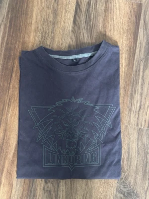 Svart Linköping T-shirt med lejon -  svart T-shirt med stort lejontryck och texten 'Linköping' på framsidan. Klassisk rund hals och korta ärmar. 