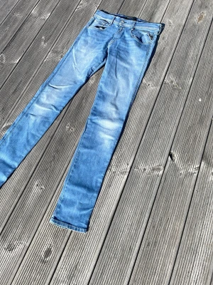 Ljusblå skinny jeans från Replay - Säljer ett par ljusblå skinny jeans från Replay med klassisk femficksdesign och snygga slitningar. Jeansen har låg midja och smal passform som sitter tajt längs benen. Perfekta för dig som gillar en avslappnad men trendig stil.