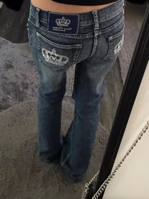 Lågmidjade Victoria Beckham jeans  - Säljer ett par blåa jeans från Victoria Beckham. Vita broderade kronor med stenar på bakfickorna, som tyvärr har börjat lossna lite. Jeansen har låg midja, lite bootcut i bena, klassisk denimlook och detaljerade sömmar. Alla mått finns på sista sidan. De är w27, men jag skulle säga att de passar XS-S. Pris kan diskuteras och skriv gärna om frågor! 💕💕💕