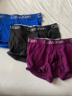 Calvin Klein 3-pack kalsonger - Säljer ett 3-pack kalsonger från Calvin Klein i färgerna blå, svart och vinröd. Klassisk boxermodell med bred resår i midjan och tydlig logga. Tillverkade i mjukt och stretchigt material för skön passform.