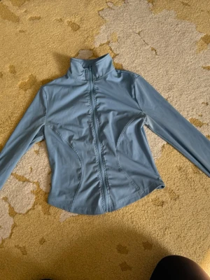 Ljusblå sportig träningsjacka - Ljusblå träningsjacka med hög krage och hel dragkedja framtill. Jackan har figurnära passform och långa ärmar. perfekt för träning eller utomhusaktiviteter.