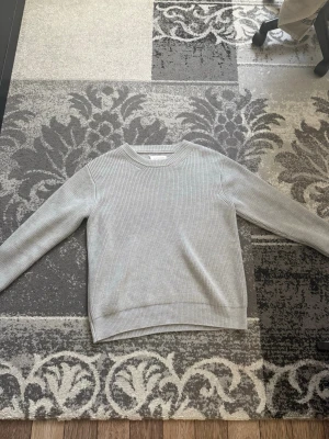 MAISON MARGIELA sweater - Säljer en stilren ljusgrå ribbstickad tröja med rund hals och långa ärmar. Tröjan har en enkel och clean design med breda muddar vid ärmslut och nederkant. Perfekt för lager på lager och passar till det mesta.