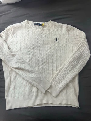 Vit kabelstickad tröja Polo Ralph Lauren - Den passar för båda L och M‼️ . Vit kabelstickad tröja från Polo Ralph Lauren med rund halsringning och broderad marinblå logga på bröstet. Tröjan har långa ärmar och ribbade muddar vid ärmslut och nederkant. Perfekt för en stilren och klassisk look.