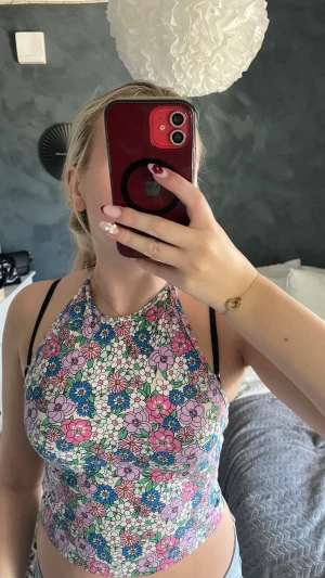 Blommig halterneck topp - Säljer en färgglad blommig halterneck topp med smala knytband i nacken. Toppen har ett mönster i rosa, blått, grönt och vitt och är croppad med en tajt passform. Perfekt för varma dagar och ger en riktigt somrig vibe!