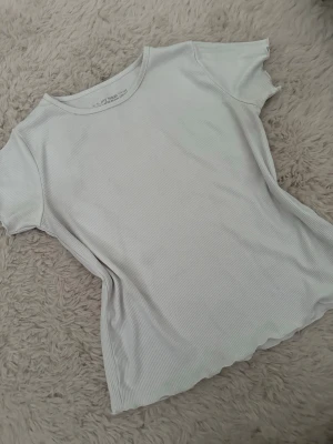 Vit ribbad t-shirt  - En enkel och stilren vit t-shirt med ribbad struktur. T-shirten har rund halsringning och korta ärmar. Perfekt basplagg att matcha med allt och superbekväm tack vare mjukt bomullsmaterial.