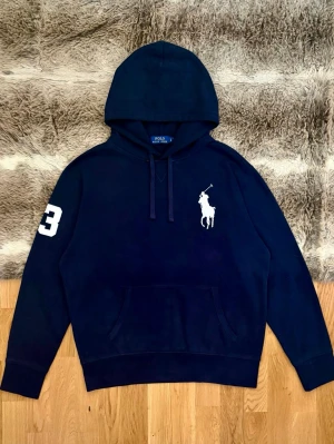Marinblå Polo Ralph Lauren Hoodie - Hej! 👋 Säljer en riktigt snygg och klassisk marinblå Polo Ralph Lauren hoodie i storlek L (Herr). Färgen är tidlös navy med den ikoniska pony-loggan broderad i vitt på bröstet 🐎 Tröjan är i mycket bra skick, välvårdad och utan några tydliga skador eller defekter ✨ Den har den välkända mjuka fleece-insidan som gör den sjukt bekväm. Personen på bilden är ca 177cm lång och väger runt 67kg👕 Alla invändiga tvättlappar sitter kvar ✅ Fraktar snabbt! 🚛📦 Hör av dig vid frågor! 💬💯 