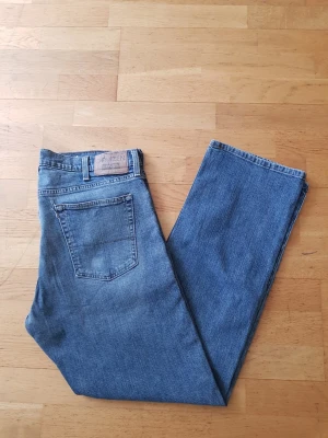 Blå raka jeans från Levi's Denizen - Säljer ett par klassiska blå jeans från Levi's Denizen med rak passform och femficksmodell. Jeansen har en snygg tvättad look och är tillverkade i slitstark denim. Perfekta för dig som gillar tidlös stil och enkel design.