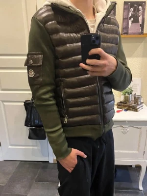 Grön pufferjacka från Moncler - Snygg grön cardigan från Moncler med quiltad front och rygg i glansigt material samt stickade ärmar och sidor. Jackan har dragkedja framtill, fickor med dragkedja och en Moncler-logga på ärmen. Perfekt för kalla dagar och riktigt trendig look.