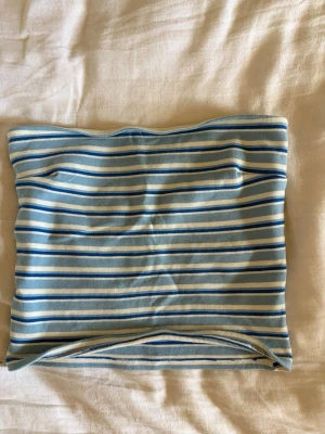 Randig blå tubtopp - Säljer en snygg randig tubtopp i ljusblått, vitt och mörkblått. Toppen är axelbandslös och har en bandeauformad passning som sitter tight.