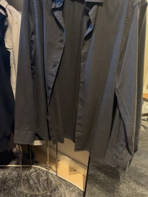 Mörkgrå skjorta från Riley Slim Fit - Stilren mörkgrå skjorta från Riley i slim fit-modell. Skjortan har klassisk krage, knappar framtill och långa ärmar med manschett. Perfekt för dig som gillar en enkel men snygg look.