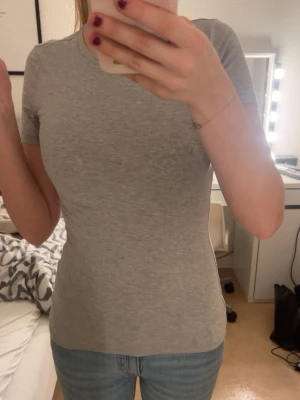 Ljusgrå t-shirt - Säljer en ljusgrå t-shirt med rund hals och korta ärmar. T-shirtens material är bomull och den sitter skönt och bra intill kroppen. Aldrig använd då jag ej gillar gråa kläder och köpte inte den själc