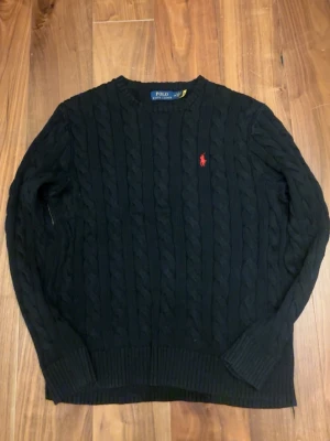 Svart kabelstickad tröja Polo Ralph Lauren - Kabelstickad svart tröja från Polo Ralph Lauren med rund halsringning och röd broderad logga på bröstet. Tröjan har långa ärmar och ribbade muddar vid ärmslut och nederkant. Perfekt för dig som gillar klassisk och stilren design. Storleken är M men jag skulle säga att den går mot M/LSkriv om ni vill ha mera bilder eller något så löser jag🤗. Priset är ej hugget i sten.