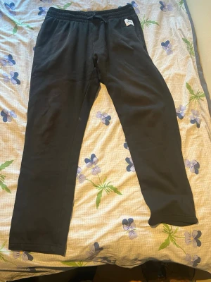 Svarta mjukisbyxor från H&M - Säljer ett par svarta mjukisbyxor från H&M med resår i midjan och dragsko för skön passform. Byxorna har raka ben och är tillverkade i mjukt bomullsmaterial. Perfekta för chill dagar eller när du vill vara bekväm.