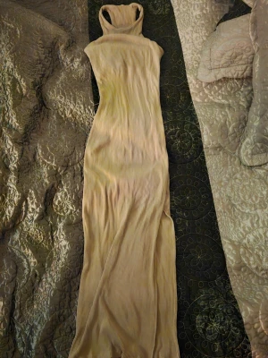 Beige ribbad långklänning - Långklänning i beige ribbat material med hög hals och ärmlös design. Klänningen har en kroppsnära passform och mjukt stretchigt tyg som ger en snygg siluett. Perfekt för dig som gillar minimalistisk och stilren look.