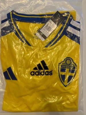 Sverige VM marchtröja Helt ny! - Helt ny! Gul matchtröja från Adidas med Sveriges landslagsmärke på bröstet och blå detaljer vid krage och axlar. Tröjan har Adidas-logga i svart och klassiska ränder på axlarna. Perfekt för fotbollsfans som vill stötta Sverige.