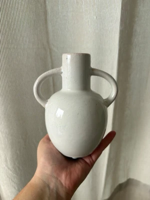 Vit keramikvas med två handtag - Stilren vit vas i keramik från Lagerhaus med två rundade handtag på sidorna. Vasen har en klassisk form med smal hals och bredare kropp, perfekt som dekoration . Passar snyggt i hyllan eller på bordet.