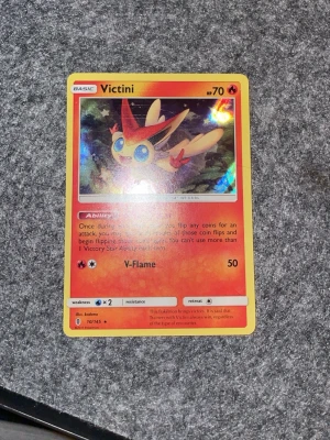 Pokémonkort Victini holo - Säljer ett Pokémonkort med Victini-motiv, holoeffekt och röda samt gula färger. Kortet har attacken V-Flame och är nummer 10/145. Perfekt för samlare eller dig som gillar Pokémonkort.