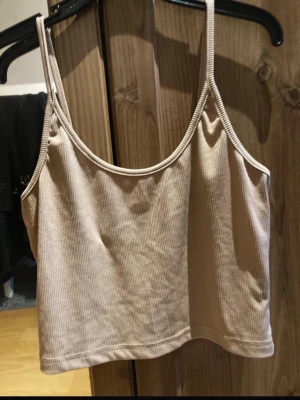 Beige ribbad croppad linnetopp - Säljer en beige croppad linnetopp med smala axelband och ribbad struktur. Perfekt för sommaren och enkel att matcha med olika stilar. Materialet känns mjukt och stretchigt.