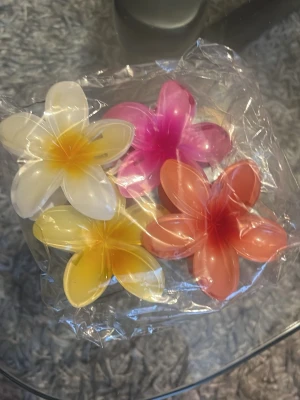 Färgglada blomformade hårklämmor - Fyra hårklämmor i form av blommor i färgerna vit, rosa, gul och orange. Tillverkade i plast med glansig finish och tydliga blomblad. Perfekta för att ge en lekfull touch till frisyren.
