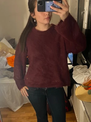 Vinröd fluffig stickad tröja - Mysig vinröd stickad tröja med fluffig yta och avslappnad passform. Tröjan har rund halsringning och långa ärmar, perfekt för kyligare dagar. Passar dig som gillar en enkel men trendig look.