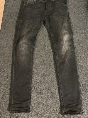 Svarta skinny jeans med slitningar - Säljer ett par svarta skinny jeans med diskreta slitningar på låren och klassisk femficksdesign. Jeansen har smal passform och är tillverkade i stretchigt denimtyg för extra komfort. Perfekta för en trendig och avslappnad look.