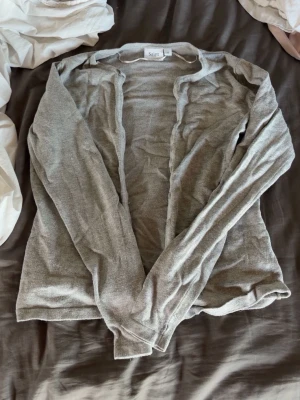 Ljusgrå cardigan från Saint Tropez - Ljusgrå tunnstickad cardigan från Saint Tropez i storlek XS. Klassisk modell med långa ärmar och knappslå framtill. 