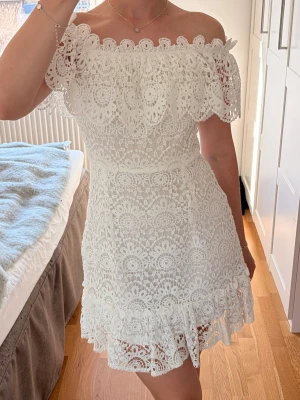 Vit spetsklänning  - Superfin vit kortklänning i spets med offshoulder och volangdetaljer. Perfekt till sommarens och studenten. Helt ny med lapp kvar, aldrig använd.