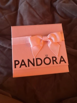 Rosa presentask från Pandora - Söt rosa presentask från Pandora med dekorativ rosett på locket och tydlig logga framtill. Asken är tillverkad i hård kartong och har en insida med silkespapper och mindre ask inuti, perfekt för att ge bort smycken.