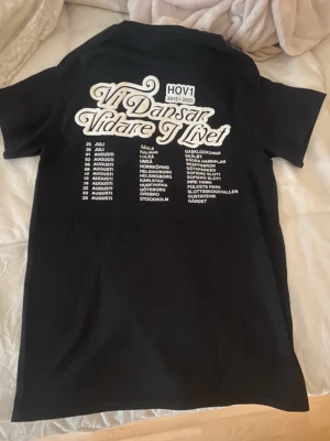 Svart Hov1 t-shirt med turnétryck! - Säljer en svart t-shirt från Hov1 med liten krona broderad framtill och stort turnétryck på ryggen med texten 'Vi Dansar Vidare I Livet' och turnédatum. Aldrig använd och det finns inga fläckar eller hål!