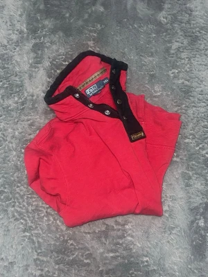 Polo Ralph Lauren Quarter-Snap Sweatshirt - Klassisk och rejäl sweatshirt från Polo Ralph Lauren med knappar i halsen. Tröjan har snygga kontrasterande detaljer vid kragen och en praktisk bröstficka med knapp. Tillverkad i en mjuk och kraftig kvalitet som håller värmen på kalla sommar kvällar. • Skick: Mycket fint skick. 