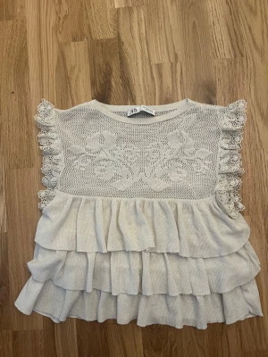 Vit volangtop från Zara - Supersöt vit topp från Zara med volanger och spetsdetaljer på ärmarna. Toppen har broderat blommönster framtill 