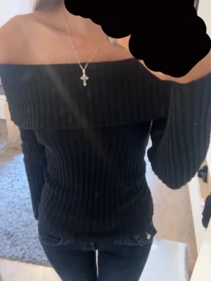 Svart off shoulder tröja - Trendig svart ribbstickad tröja med off shoulder-design och långa ärmar. Ger en snatched look som framhäver siluetten. Perfekt att matcha med jeans. Materialet är skönt och ganska stretchigt.