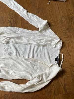 Vit tunn kofta med knappar - Säljer en vit, tunn och lätt kofta med knäppning framtill. Koftan har långa ärmar och en enkel, stilren design som passar perfekt till lager på lager. Materialet känns mjukt och luftigt, vilket gör den skön att bära.