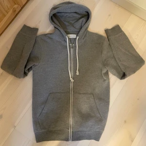 ZIP-HOODIE | PIER ONE. - Klassisk grå hoodie med dragkedja framtill och vita dragsnören i huvan. Hoodien har två stora fickor på magen och ribbade muddar vid ärmslut och nederkant. Perfekt för en avslappnad och chill stil.