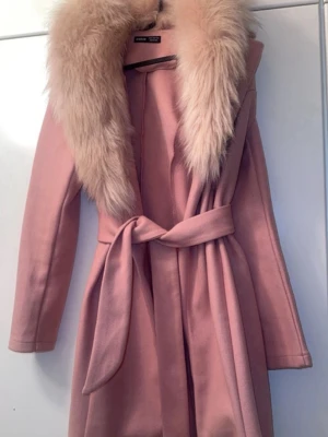 Rosa kappa - Snygg rosa kappa från Shein med bred krage i ljus fuskpäls och knytskärp i midjan. Kappan har en klassisk, rak passform och är tillverkad i ett mjukt tyg som ger en lyxig känsla. Perfekt för dig som vill sticka ut med stil.
