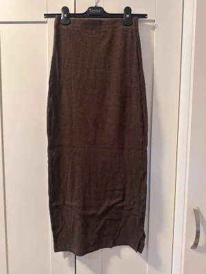 Brun ribbad långkjol - Säljer en brun långkjol med ribbad struktur. Kjolen har en rak passform och slits nertill för extra rörelsefrihet. Perfekt att styla med en enkel topp eller stickad tröja.