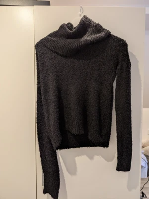 Svart fluffig polotröja stickad - Mysig svart stickad polotröja med fluffig textur och lång ärm. Tröjan har en bred polokrage och är tillverkad i ett mjukt, luddigt material som känns skönt mot huden. Perfekt för kyliga dagar och enkel att matcha med olika outfits. Det står varken storlek eller märke vad jag kan se men de passar lite oversized på mig som normalt har S,SX
